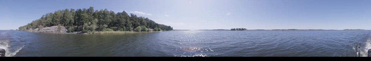 Green forests flank a wide lake in Upplands-Bro, Sweden. This daytime boat perspective features a clear summer sky and sunlight reflecting on the water.