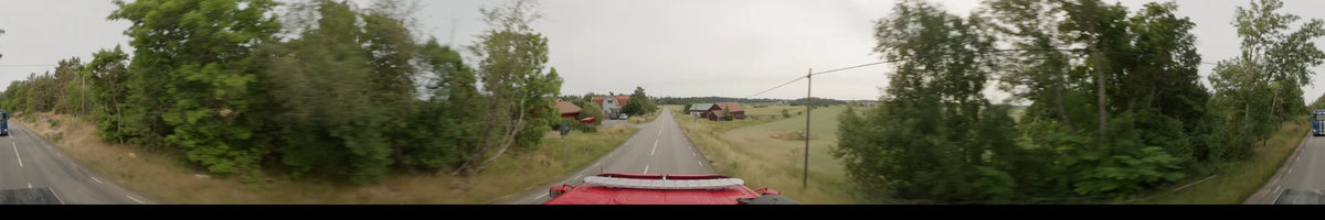 POV shot from a bus driving through Märsta, Sweden, on an overcast summer morning, passing green fields and traditional red wooden houses along a rural road.