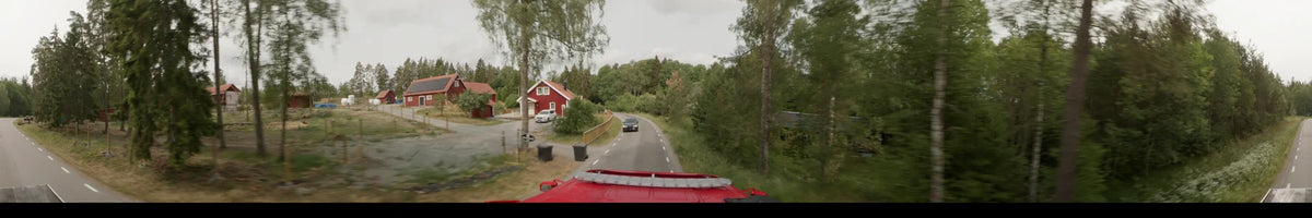 Viewed from a bus, a red house and an oncoming black car appear along a winding road in Märsta, Sweden, on an overcast summer morning.