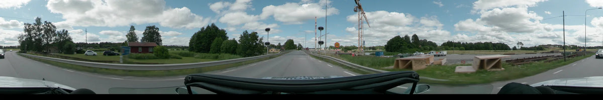 A road bridge in Upplands-Bro features railway crossing signals and a construction crane against a partly cloudy sky, with green trees and a small building nearby.