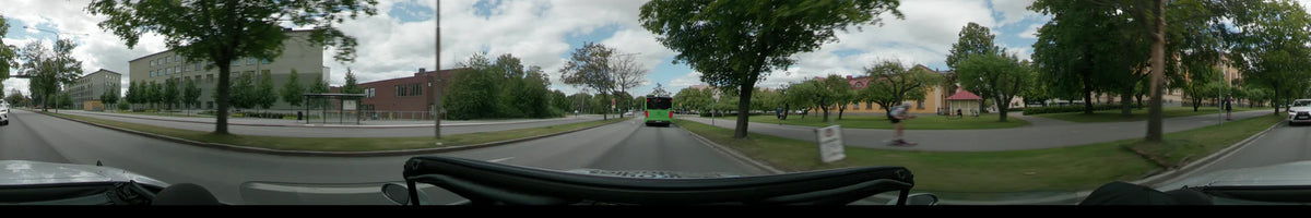 A green bus drives ahead on a road in Uppsala, bordered by lush green trees and a pedestrian path under a partly cloudy sky.