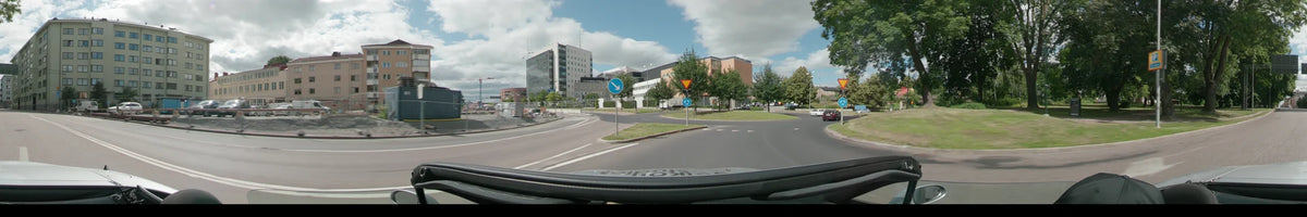 Modern office buildings and blue traffic signs line a wide asphalt road in Uppsala, with green trees and a few distant cars under a partly cloudy sky.