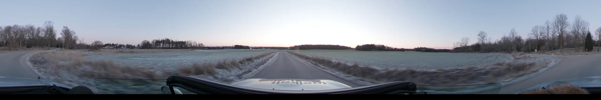 Frosty fields border a paved road in Lennartsnäs, Sweden, while a car drives toward a distant forest under a clear autumn morning sky.