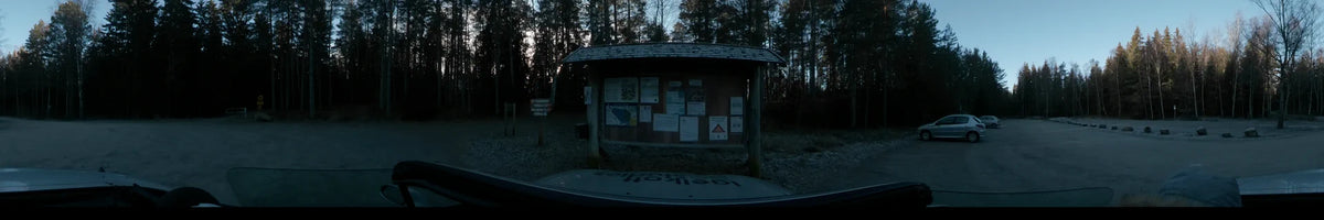 Seen from a car, a sheltered wooden information board and a signpost are positioned in a forest during a clear autumn day in Lennartsnäs, Sweden.