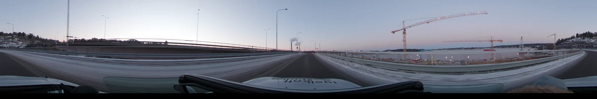 Industrial plumes rise above a snowy highway and streetlights in Stockholm, Sweden, during a clear winter dawn, as seen from a moving car.