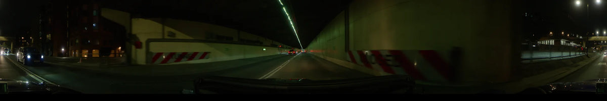 On a clear spring night in London, United Kingdom, a car follows another vehicle through a concrete tunnel beneath rows of linear lights.