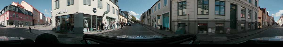 A cobblestone street lined with traditional white and yellow buildings and pedestrians in Lund, where a black car is parked along the curb.