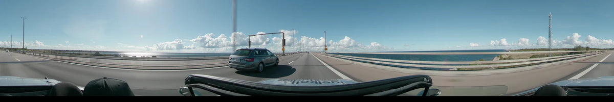 The Øresund Bridge with towering pylons and symmetric cables spans the water, with a few cars traveling ahead under a clear sky.