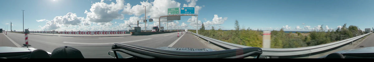 A highway with overhead signs for Copenhagen and the airport, featuring a red truck and white vans between Malmö and Copenhagen under a clear sky.