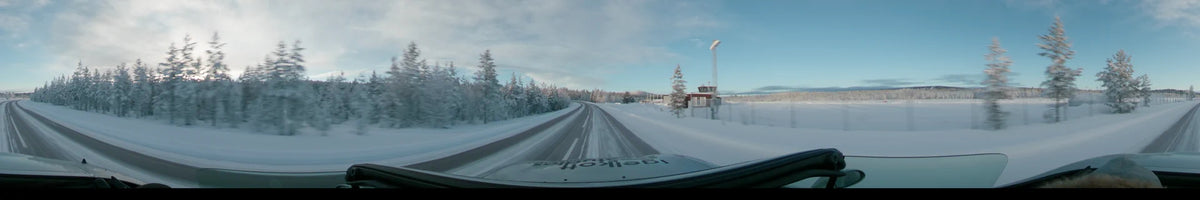 During a partly cloudy sunrise in Dalarna, Sweden, a car drives past snow-covered trees and a small airfield tower with a windsock on a winter road.
