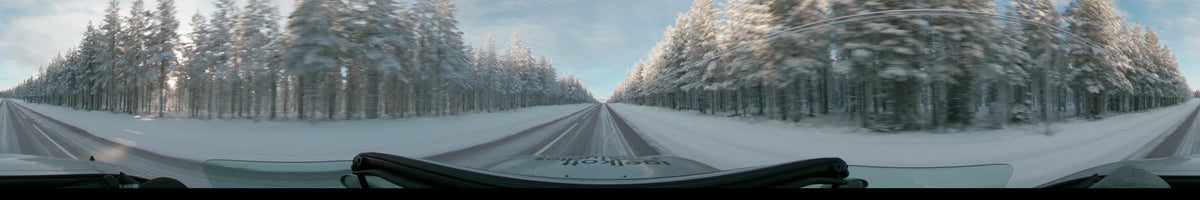 Snow-covered trees line a straight road in Dalarna, Sweden, as a car travels through the winter landscape during a partly cloudy day.