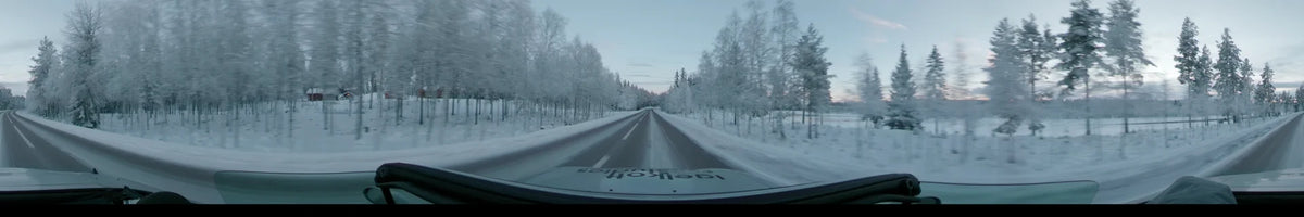 A snowy road winds through frosted forests in Dalarna, Sweden, as a car travels under a partly cloudy winter afternoon sky.