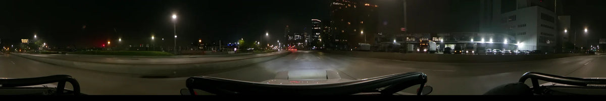 A wide road leads toward the illuminated New York skyline during a spring night in the United States. The perspective is from inside a car.