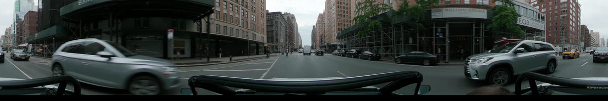 New York city traffic, scaffolding, and tall brick buildings pass by on an overcast spring day as a car follows a white van.