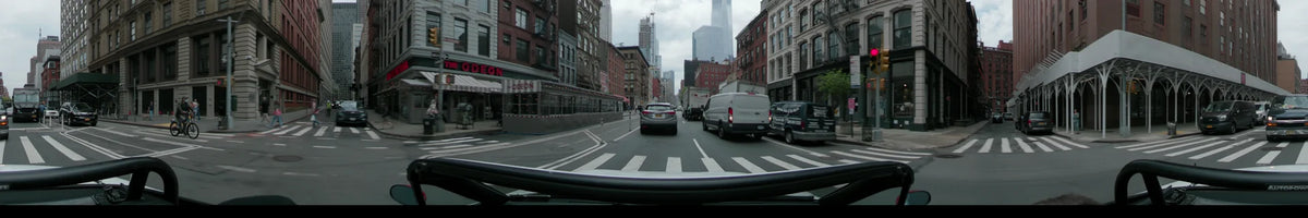 Silver and white vehicles lead the way past Odeon restaurant in New York on an overcast spring day, with tall brick buildings and skyscrapers lining the road.