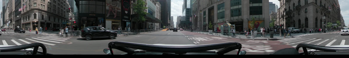 The New York Public Library and tall skyscrapers line Fifth Avenue in New York as a car follows a black SUV on a partly cloudy spring day.