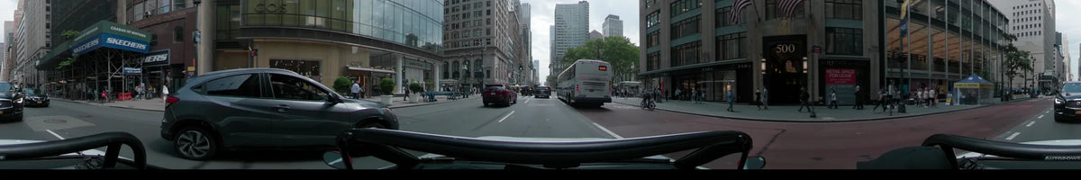 A white bus and red SUV lead a car through New York on a partly cloudy spring day, amidst towering city buildings.