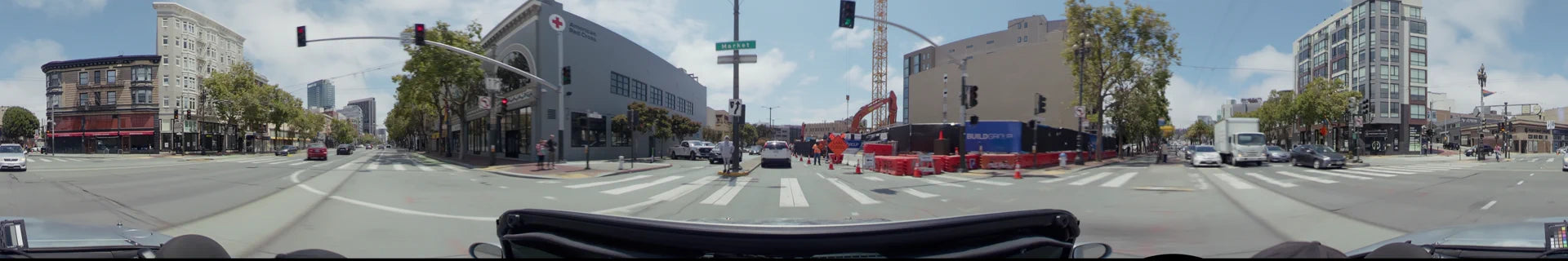 Market Street in San Francisco featuring a construction zone with orange barriers, an excavator, and a white SUV driving past a grey office building.
