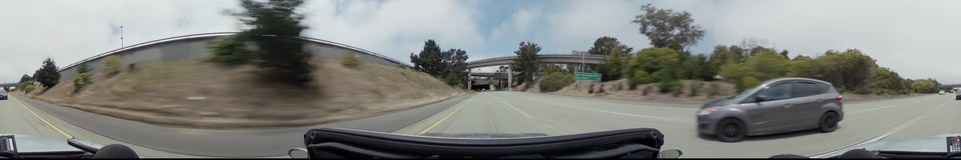 A multi-lane highway in San Francisco featuring concrete overpasses, grassy embankments, and sparse traffic under a partly cloudy sky.