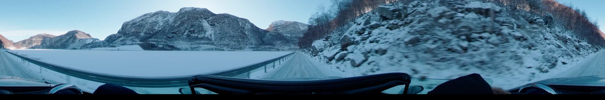 Between a frozen fjord and rocky mountains, this view from a car follows a snowy road in Stavanger, Norway, on a clear spring day.