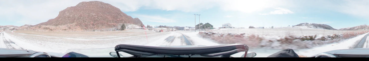 Utility poles and houses stand along a snow-covered road in this view from a car on a partly cloudy spring day in Stavanger, Norway.