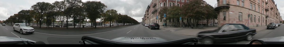 Passing traditional stone buildings and autumn trees, a car travels along a city street in Stockholm, Sweden, under an overcast sky during the day.