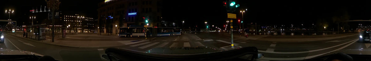 A blue bus passes across a road with a zebra crossing in Stockholm, Sweden, during a clear autumn night, as seen from a car.