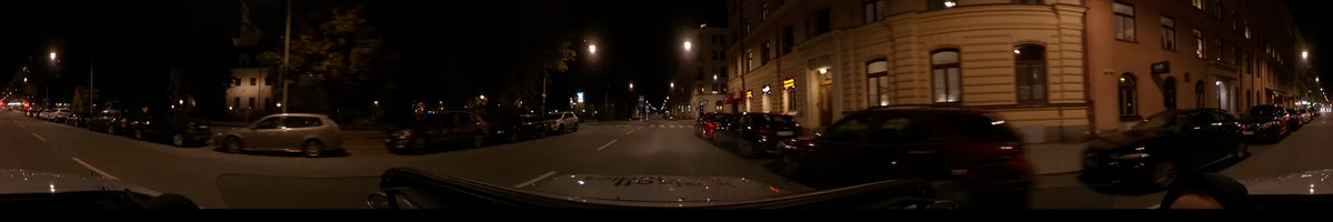 From a car, streetlights illuminate parked vehicles and city buildings along a road in Stockholm, Sweden, during a clear autumn night.