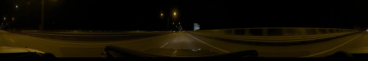 A blue E20 road sign and glowing streetlights line a highway in Stockholm, Sweden, as a car drives along on a clear autumn night.