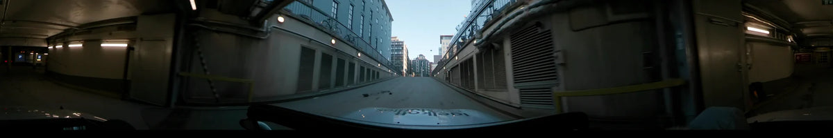 A car drives up a ramp flanked by urban buildings and concrete walls in Stockholm, Sweden, during a clear winter dawn.