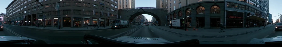 Passing a large truck, a car travels beneath a wide stone archway on a city road in Stockholm, Sweden, during a clear winter dawn.
