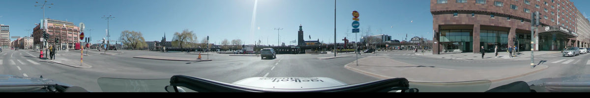 Daytime driving shot from a car in Stockholm, Sweden, during spring. The scene features a clear sky and the prominent Stockholm City Hall tower.