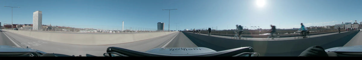 A car travels past cyclists toward the Avicii Arena in Stockholm, Sweden, on a clear spring day, with the Stockholm Waterfront Congress Centre nearby.