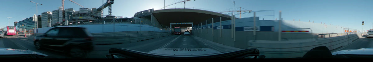 Under a concrete overpass, a red bus and white car precede a car traveling through Stockholm, Sweden, on a clear spring day.