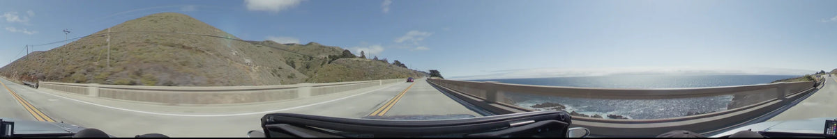 A scenic highway in Big Sur with a car approaching on a bridge, bordered by steep golden hills and the Pacific Ocean.