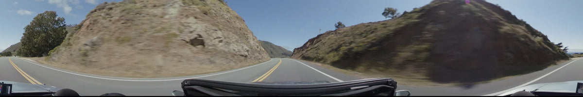 A winding road in Big Sur cuts through steep, rocky slopes and golden hills under a clear, bright sky.