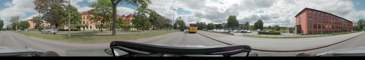 A yellow bus and a black car travel along a tree-lined road in Uppsala, with parked cars and residential buildings visible under a cloudy sky.