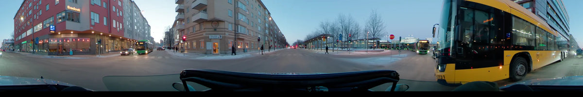 Car driving plate from Uppsala, Sweden, during a clear winter afternoon. The scene features snowy city streets, residential buildings, and a bus stop with pedestrians.