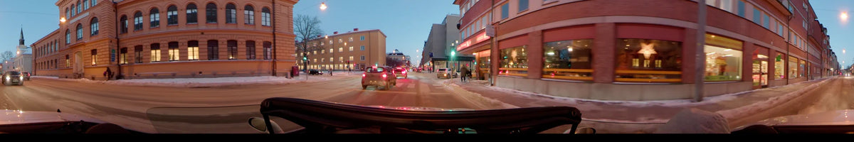 A car navigates a clear winter afternoon in Uppsala, Sweden. The street view shows snow-lined sidewalks, urban buildings, traffic lights, and pedestrians.