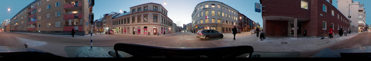 Snowy city streets in Uppsala, Sweden, during a clear winter afternoon, with a car passing multi-story buildings and another silver vehicle.