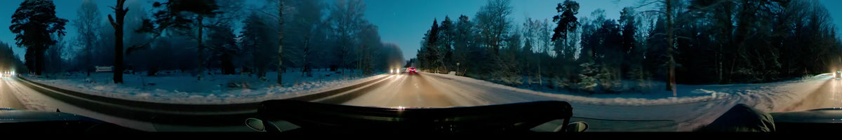 Driving through Uppsala, Sweden, on a clear winter afternoon, a car follows other vehicles along a snowy road bordered by snow-covered trees.