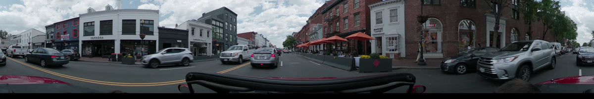 On a partly cloudy spring day in Washington, United States, a car passes brick buildings lined with orange umbrellas and outdoor seating.