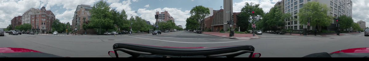 On a partly cloudy spring day in Washington, United States, a car travels past red brick buildings and green trees along a multi-lane city street.