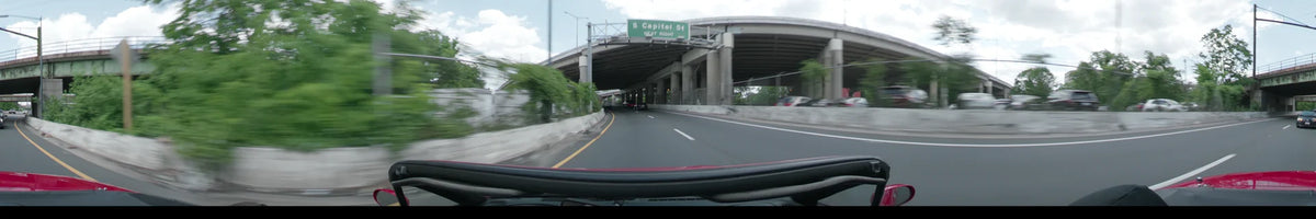 Under a concrete overpass in Washington on a partly cloudy spring afternoon, a car passes a sign for S Capitol St surrounded by lush greenery.