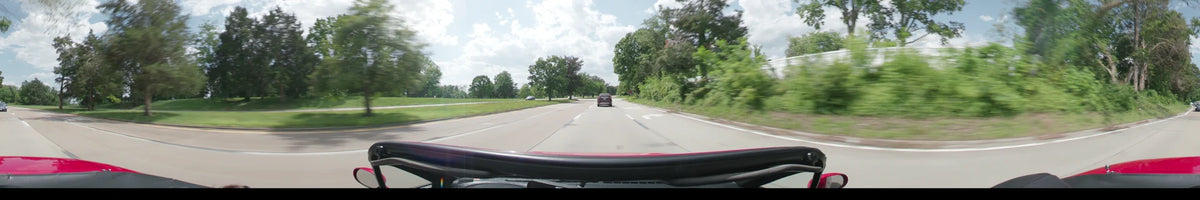 A car follows a red vehicle along a multi-lane road in Washington, bordered by green spring trees under a partly cloudy afternoon sky.