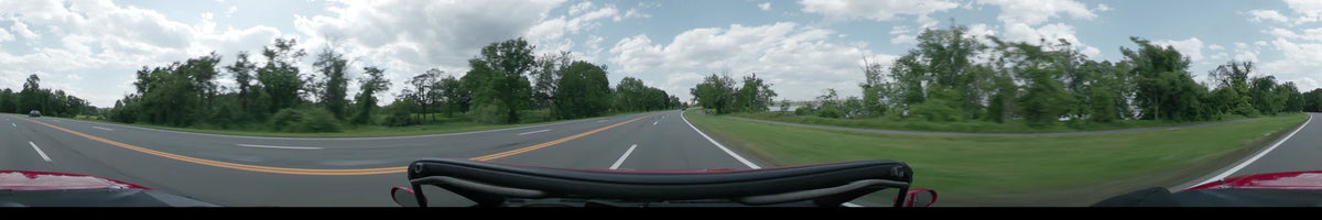 Green spring trees and a distant body of water are visible as a car drives through Washington on a partly cloudy afternoon.