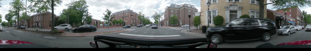 A car drives past red brick buildings and through a signaled intersection in Washington during a partly cloudy spring afternoon.