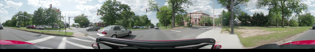 Passing through a signaled intersection at Slaters Lane, a car travels amidst spring foliage and red brick buildings during a partly cloudy afternoon in Washington.