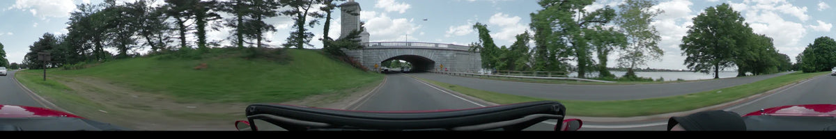 A large stone arch bridge spans the road as a car drives through green spring landscapes in Washington during a partly cloudy afternoon.