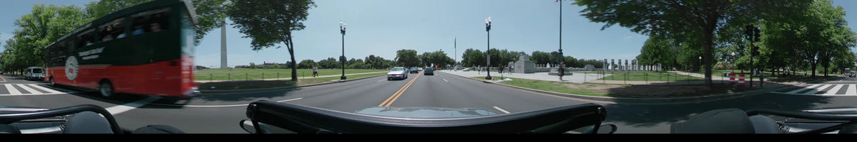 A car travels past the World War II Memorial in Washington, United States, on a clear spring day amidst lush green scenery.